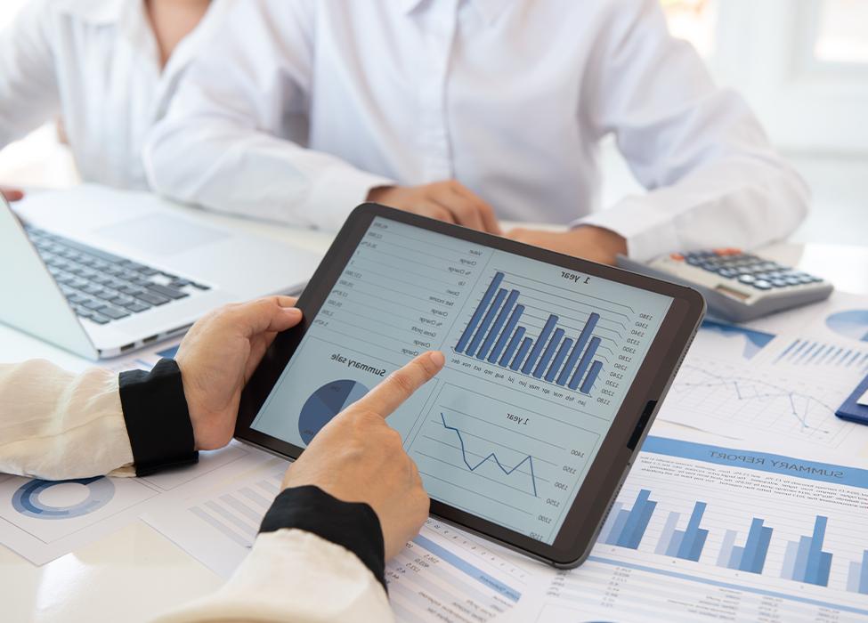 Financial Management Software | Image of three people at work sitting around a table with charts scattered around; one person holds a tablet.
